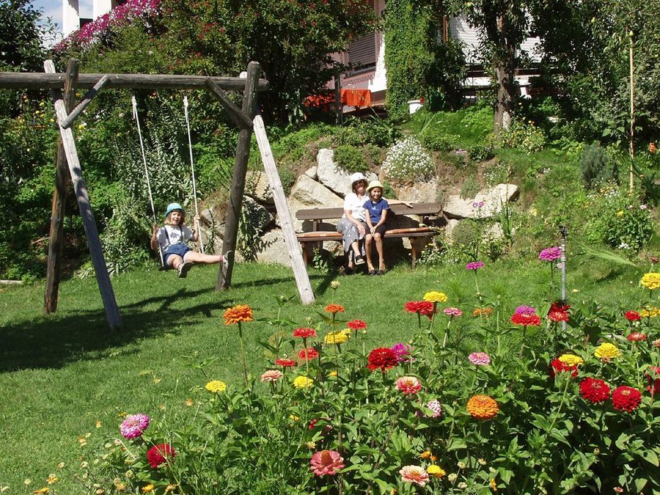 Kinder spielen und sitzen auf einer Bank in einem blumigen Garten.