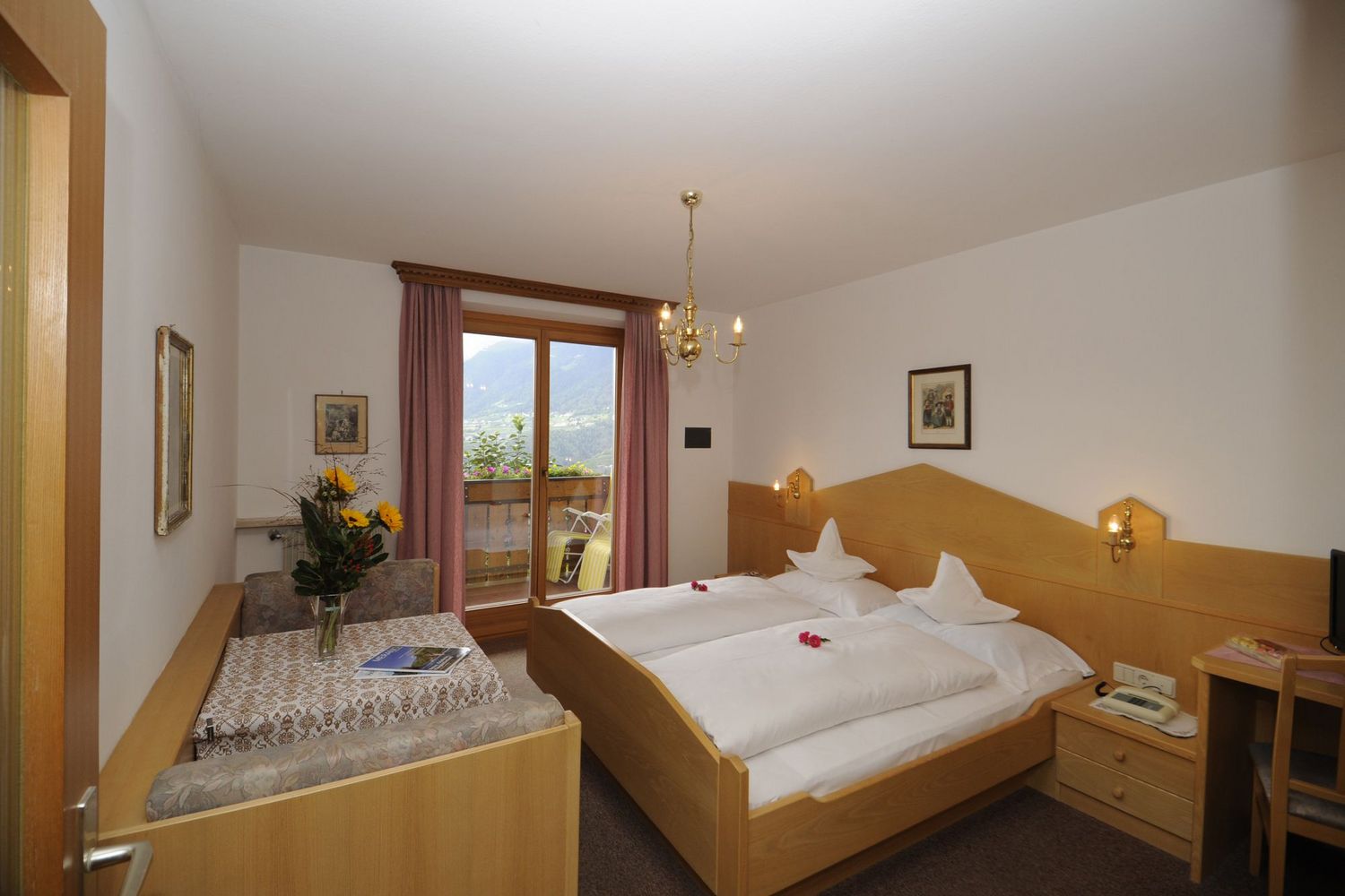 Gemütliches Hotelzimmer mit Doppelbett, Esstisch und Balkon mit Bergblick.