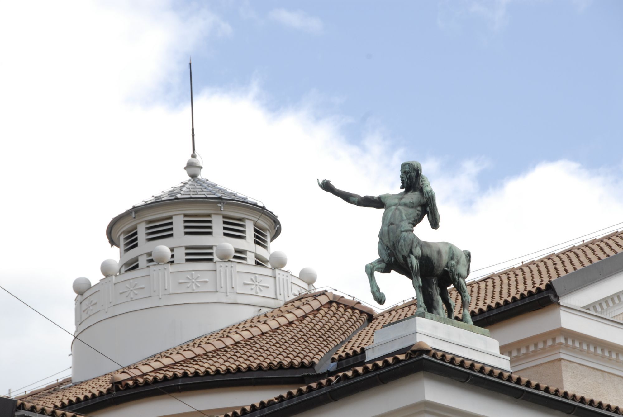 Statue eines Zentauren auf einem Gebäudedach vor blauem Himmel
