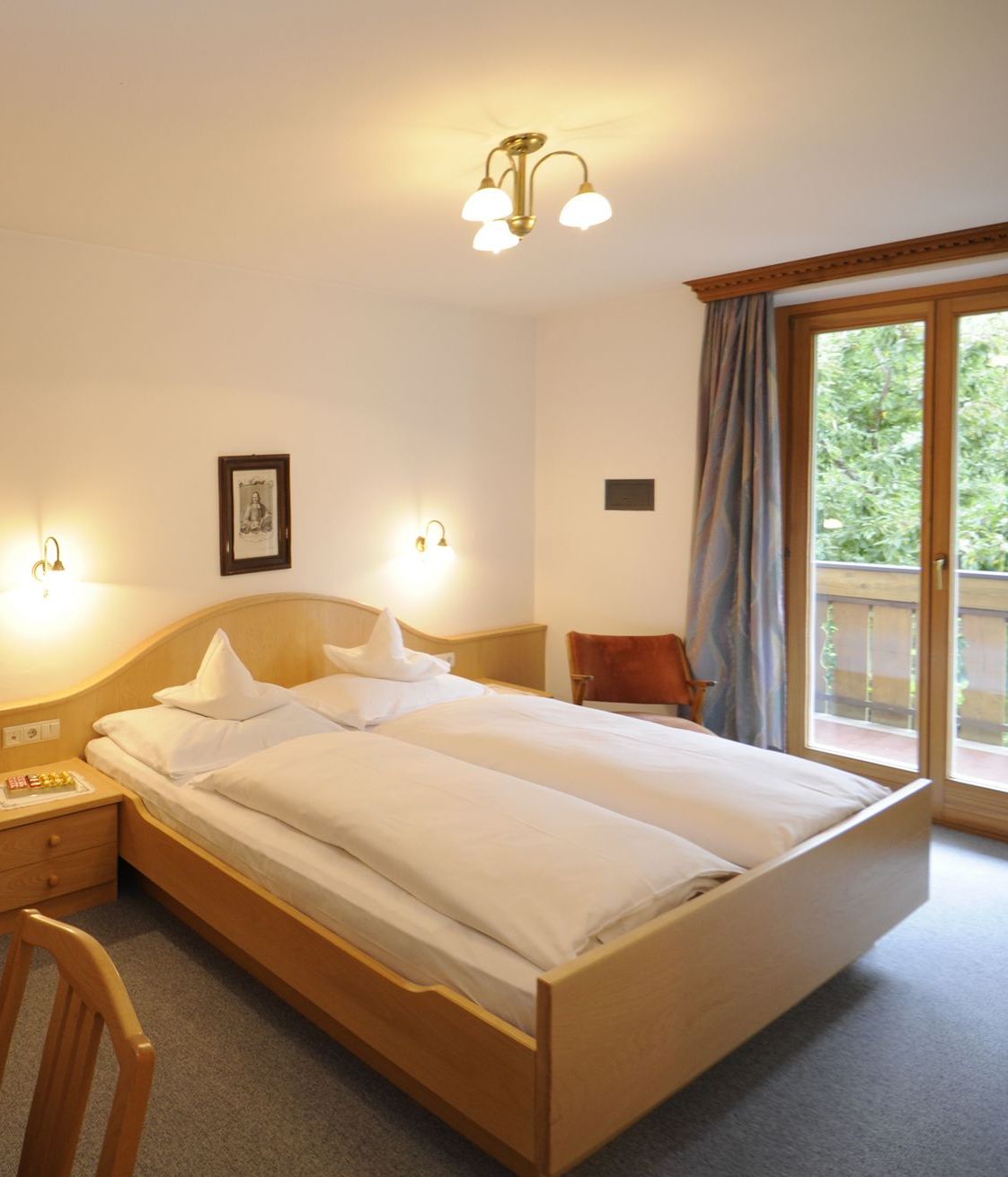 Gemütliches Schlafzimmer mit Doppelbett, Holzmöbeln und Balkon mit Blick ins Grüne.