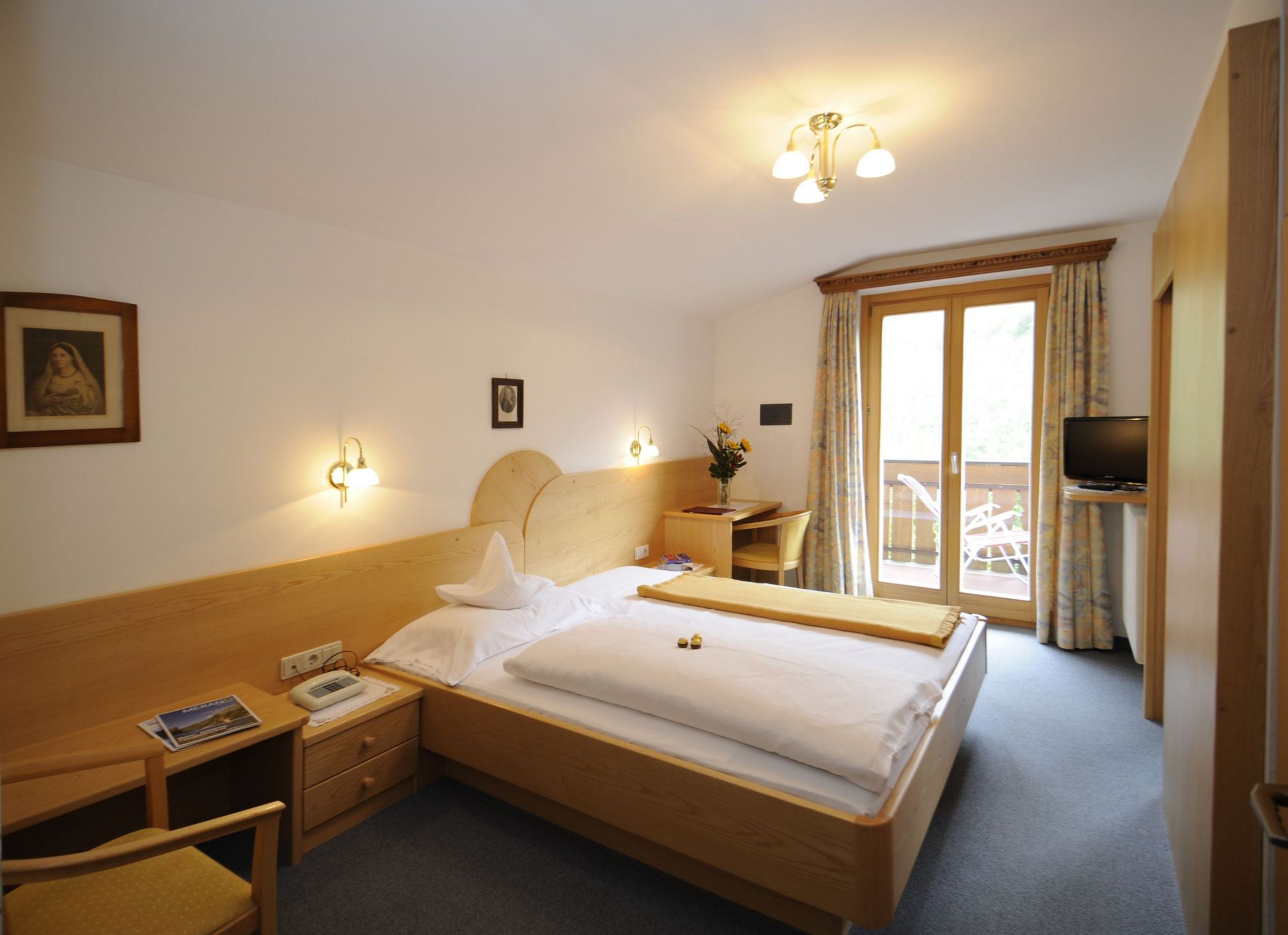 Hell eingerichtetes Hotelzimmer mit Holzmöbeln und Balkonzugang