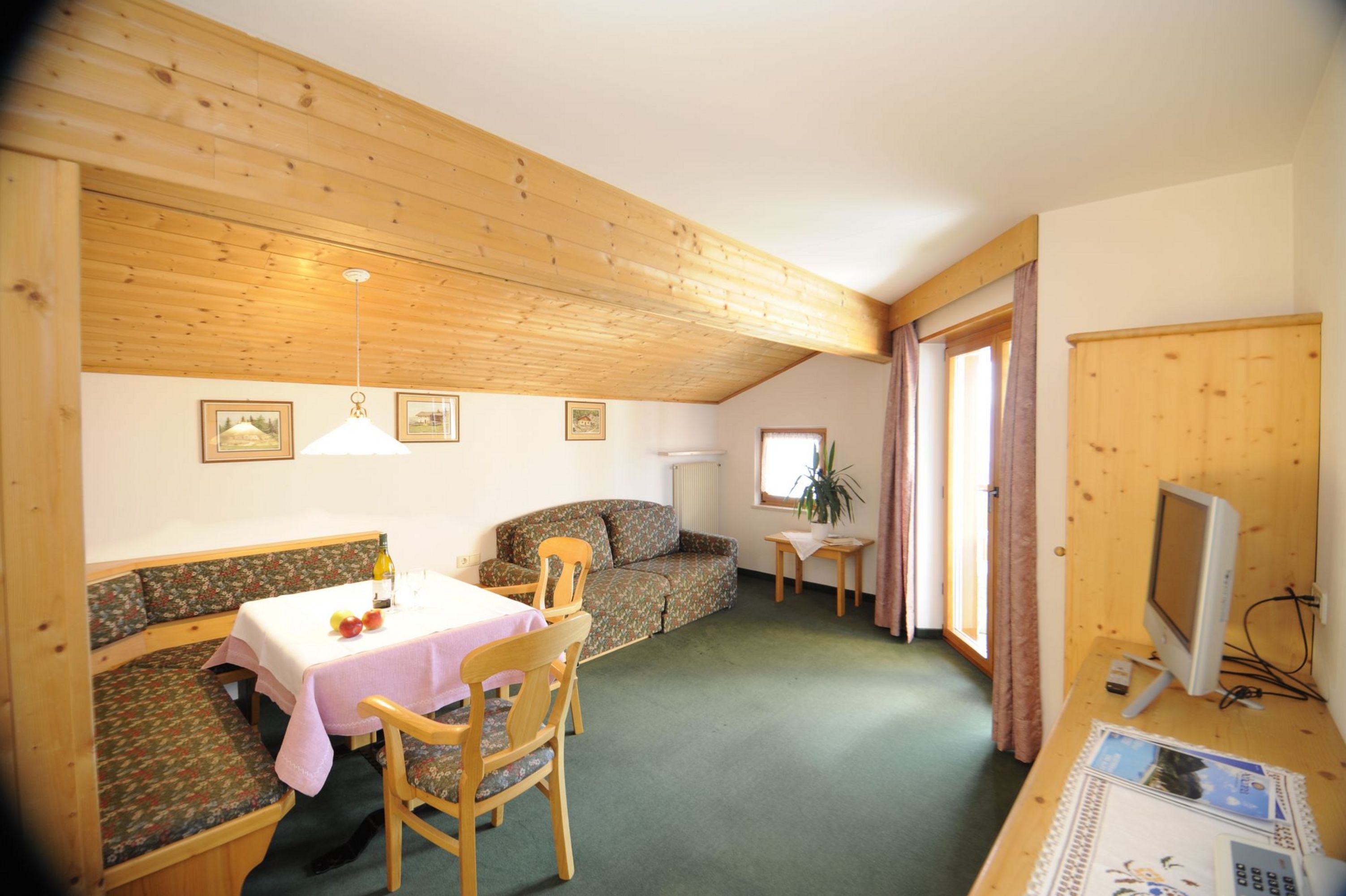 Gemütlicher Wohnbereich mit Holzverkleidung, Esstisch, Sofa und Fernseher.