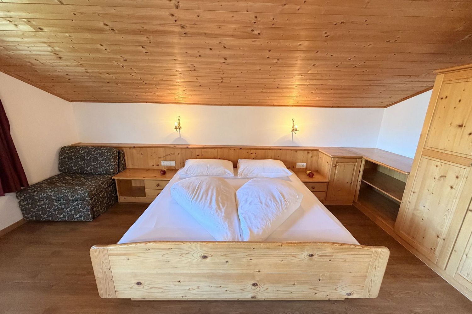 Ein Schlafzimmer unter einer Dachschräge mit einem Holzbett, weißen Bettdecken, einem gemusterten Sessel und Holzschränken.