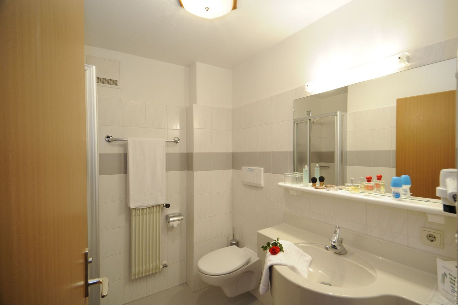 Modernes Badezimmer mit Toilette, Waschbecken, Spiegel und Handtuch mit roter Rose.
