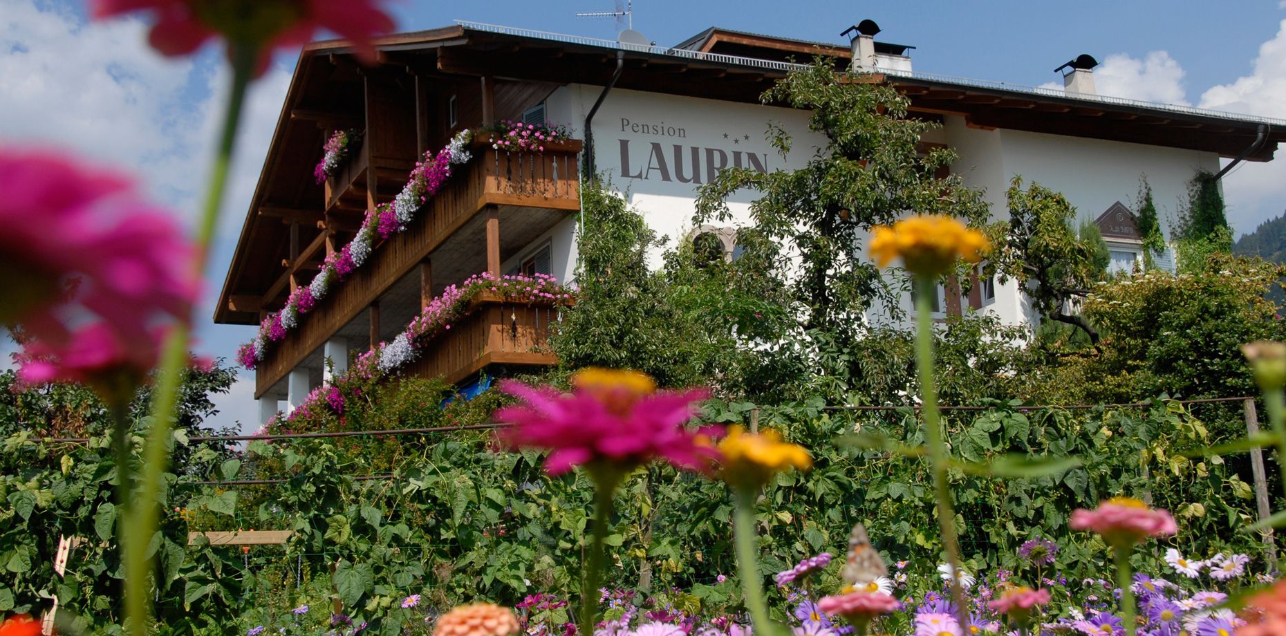 Pension Laurin mit blumengeschmückten Balkonen und Blumen im Vordergrund