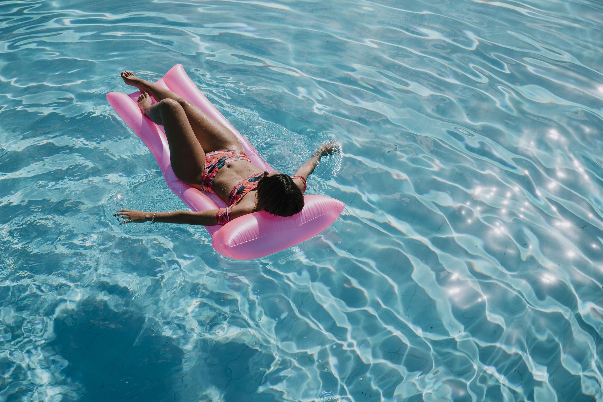Frau entspannt auf pinkem Luftmatratze im Pool